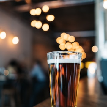 Head brewer inspecting a glass of beer beside towering copper brew kettles